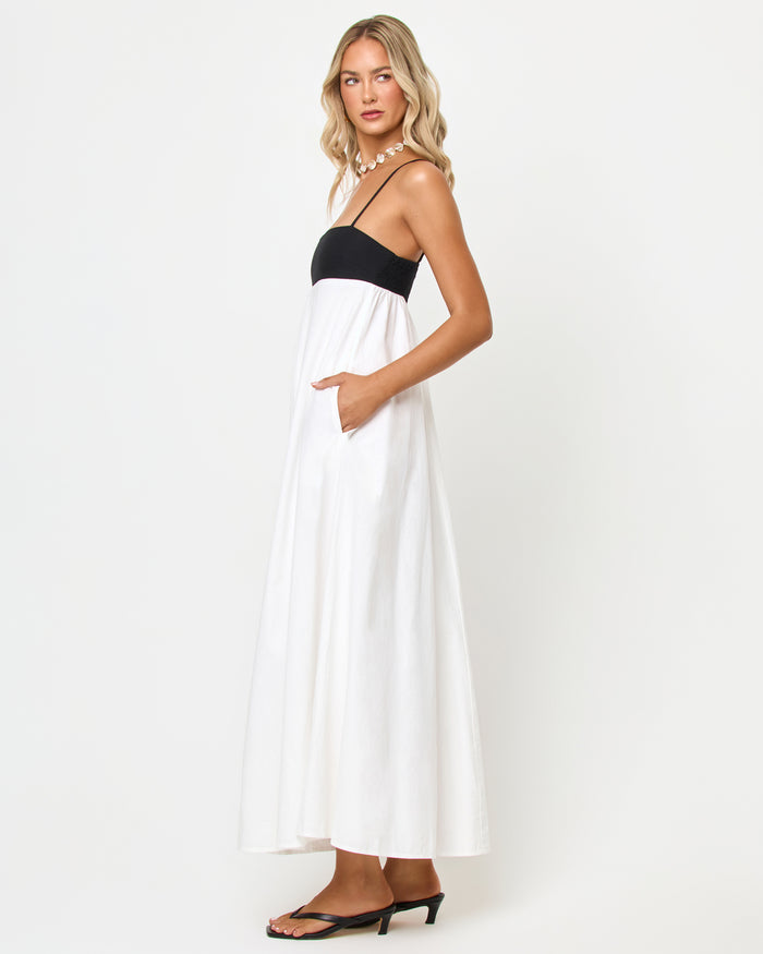 Side view of a model wearing the LSPACE Raveena Dress in black-cream, showing the empire-waist silhouette with a black bodice, spaghetti straps, and a flowing cream maxi skirt.