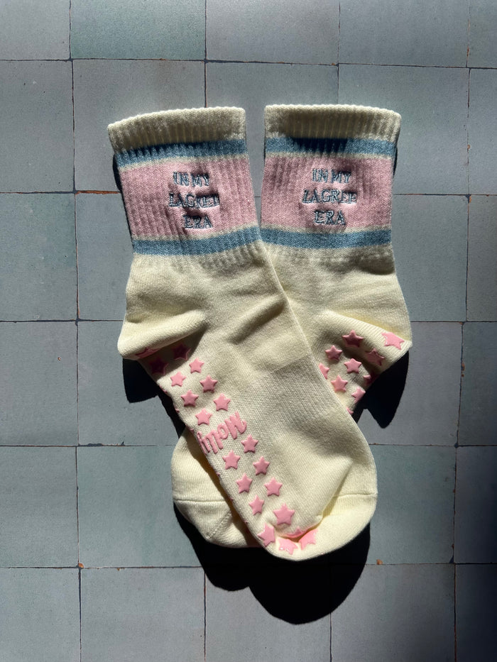 Cream pilates non slip grip sock with pink and blue stripes and pink star grips.  "in my lagree era" is embroidered on them. Used for Pilates, yoga, lagree and barre