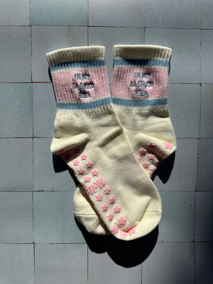 Cream pilates non slip grip sock with pink and blue stripes and pink star grips.  "in my lagree era" is embroidered on them. Used for Pilates, yoga, lagree and barre