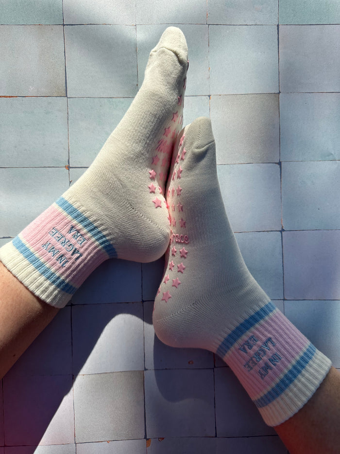 Cream pilates non slip grip sock with pink and blue stripes and pink star grips.  "in my lagree era" is embroidered on them. Used for Pilates, yoga, lagree and barre
