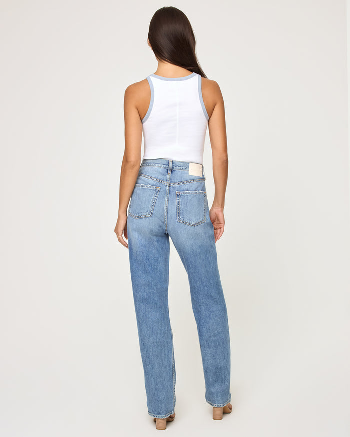 Back view of a model wearing the LSPACE Rewind Tank in salty cowgirl, a white ribbed tank with blue contrast trim at the neckline and armholes, showing the clean back and racerback-style cut, styled with straight-leg jeans.