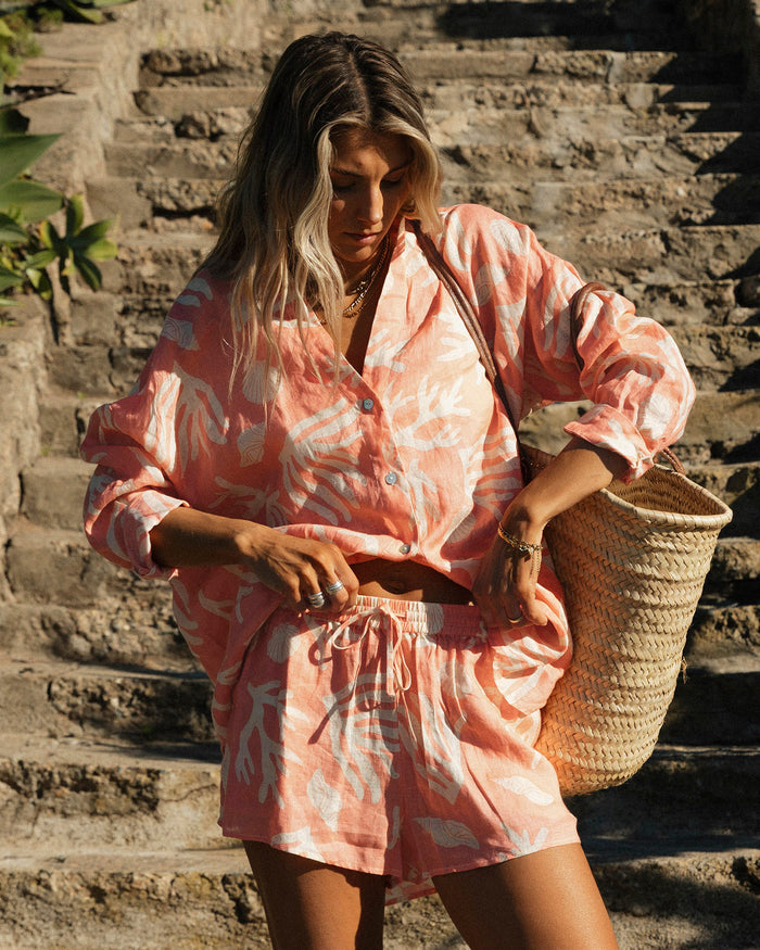 Front view of a model wearing the LSPACE Rio Short in shell or high water, a linen short with a coral and white tropical leaf print and elastic drawstring waistband, styled with the matching Rio Tunic.