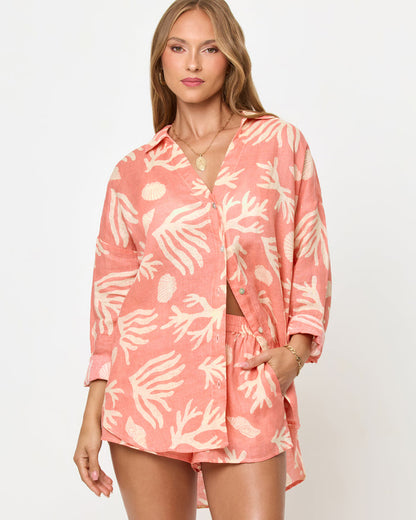 Front view of a model wearing the LSPACE Rio Tunic in shell or high water, a coral linen button-up shirt with a cream tropical seashell and coral print, styled with the matching Rio Short.