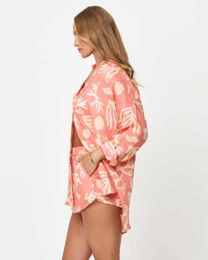 Side view of a model wearing the LSPACE Rio Tunic in shell or high water, showing the relaxed linen button-up silhouette with a coral and cream tropical seashell and coral print, styled with the matching Rio Short.