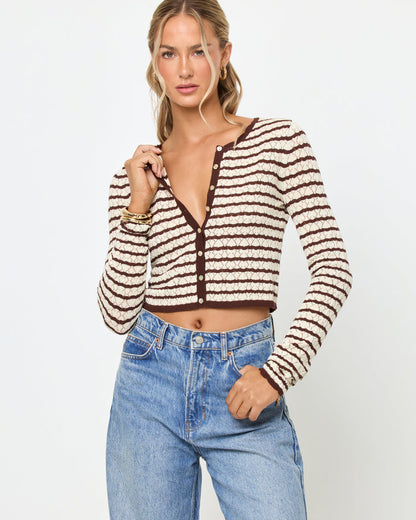 Front view of a model wearing the LSPACE Rosalie Cardigan in cafe-cream, a cropped knit cardigan with cream and dark brown horizontal stripes, a V-neckline, and gold button closure, styled with light wash jeans.