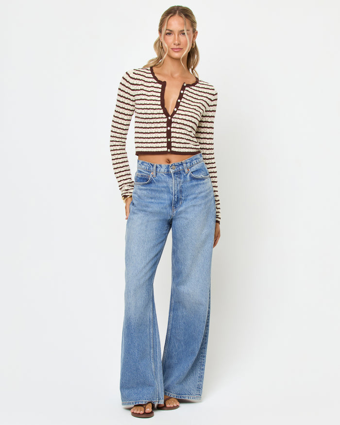 Front view of a model wearing the LSPACE Rosalie Cardigan in cafe-cream, a cropped knit cardigan with cream and dark brown horizontal stripes, a V-neckline, and gold button closure, styled with wide-leg light wash jeans.