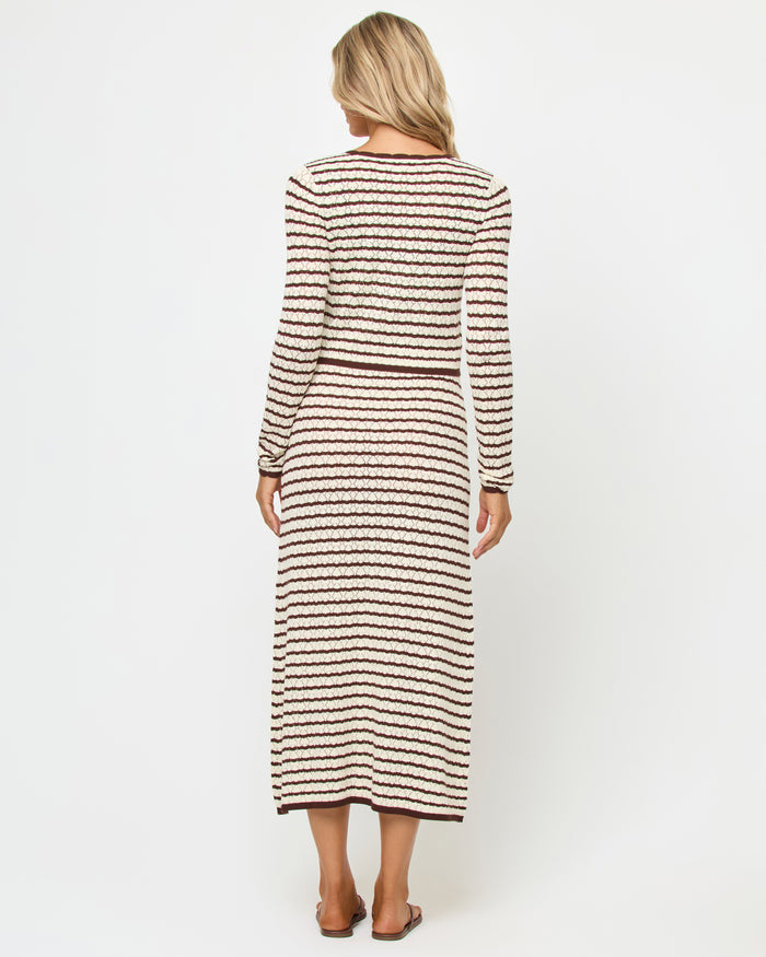 Back view of a model wearing the LSPACE Rosalie Cardigan in cafe-cream, a cropped knit cardigan with cream and dark brown horizontal stripes, styled with the matching Rosalie Maxi dress.