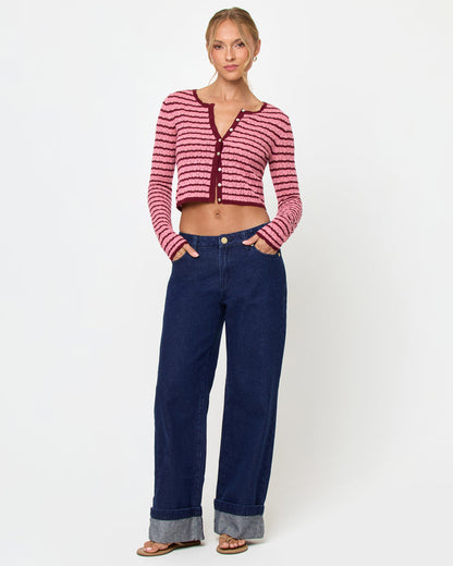 Front view of a model wearing the LSPACE Rosalie Cardigan in strawberry stripe, a cropped knit cardigan with pink and burgundy horizontal stripes, a V-neckline, and gold button closure, styled with wide-leg dark wash jeans and sandals.
