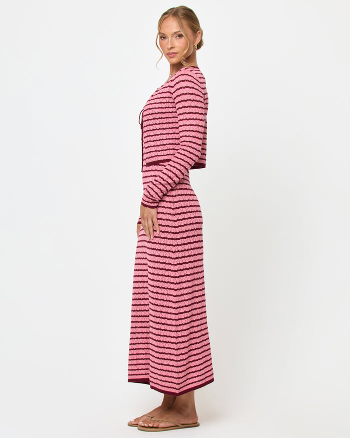 Side view of a model wearing the LSPACE Rosalie Cardigan in strawberry stripe, a cropped knit cardigan with pink and burgundy horizontal stripes, styled with the matching Rosalie Maxi dress.