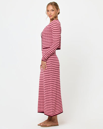 Side view of a model wearing the LSPACE Rosalie Cardigan in strawberry stripe, a cropped knit cardigan with pink and burgundy horizontal stripes, styled with the matching Rosalie Maxi dress.