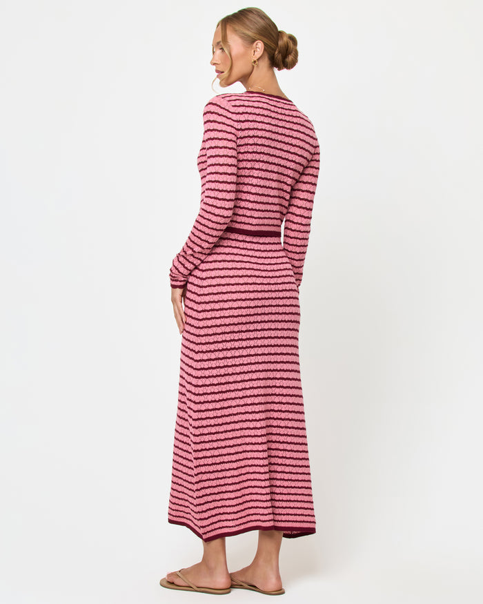 Back view of a model wearing the LSPACE Rosalie Cardigan in strawberry stripe, a cropped knit cardigan with pink and burgundy horizontal stripes, styled with the matching Rosalie Maxi dress.