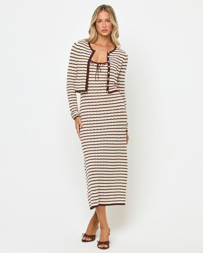Front view of a model wearing the LSPACE Rosalie Maxi in cafe-cream, a fitted sleeveless knit maxi dress with cream and dark brown horizontal stripes and lace-up tie neckline, styled with the matching Rosalie Cardigan and brown heels.