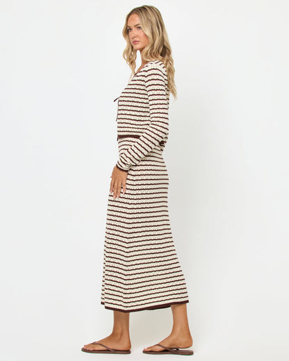 Side view of a model wearing the LSPACE Rosalie Maxi in cafe-cream, a fitted sleeveless knit maxi dress with cream and dark brown horizontal stripes, styled with the matching Rosalie Cardigan and brown sandals.