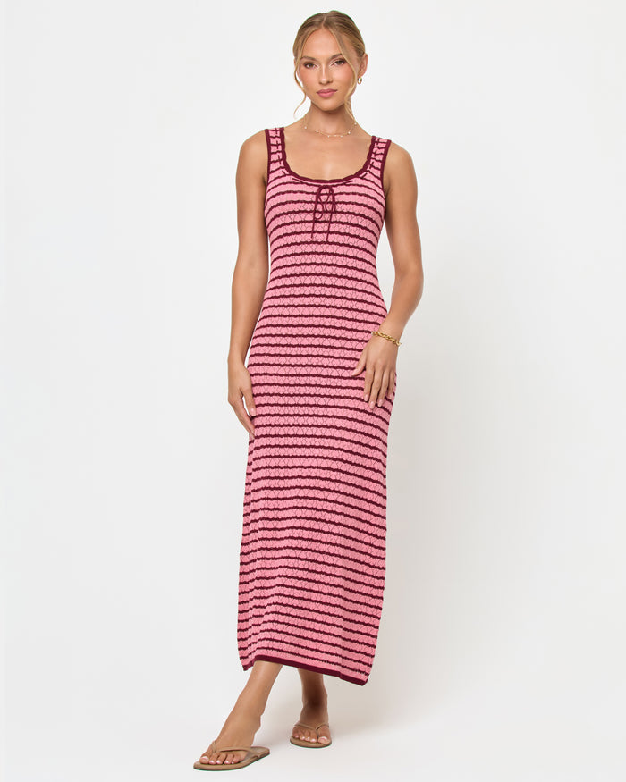 Front view of a model wearing the LSPACE Rosalie Maxi in strawberry stripe, a fitted sleeveless knit maxi dress with pink and burgundy horizontal stripes, a scoop neckline with lace-up tie detail, styled with sandals.