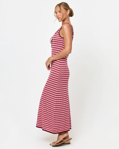 Side view of a model wearing the LSPACE Rosalie Maxi in strawberry stripe, a fitted sleeveless knit maxi dress with pink and burgundy horizontal stripes and a lace-up tie at the neckline.