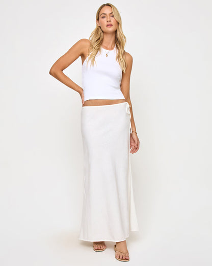 Front view of a model wearing the LSPACE Stop and Stare Skirt in cream, a flowing maxi skirt with a low waist and side tie button closure, styled with a white halter crop top.