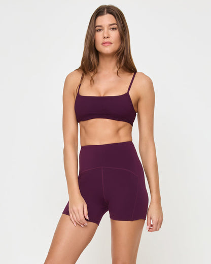 Front view of the LSPACE Stride Bra in plum on a model against a white background, paired with matching plum high-waist active shorts, showing the profile silhouette.