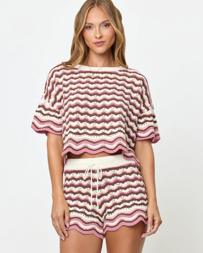 Front view on model of the LSPACE Sunchaser Short in Neapolitan, a crochet mini short in a brown, pink, and white wave pattern with drawstring waist and scalloped hem, styled as a set with the matching Sunchaser Top.