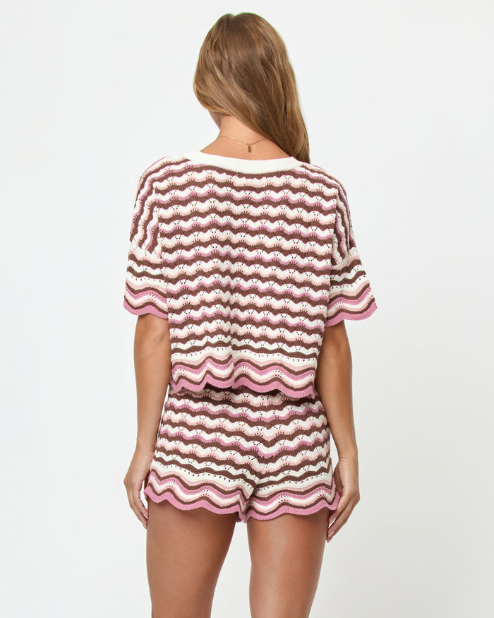 Back view on model of the LSPACE Sunchaser Short in Neapolitan, a crochet mini short in a brown, pink, and white wave pattern with scalloped hem, styled as a set with the matching Sunchaser Top.