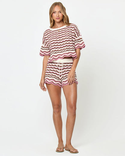 Front view on model of the LSPACE Sunchaser Short in Neapolitan, a crochet mini short in a brown, pink, and white wave pattern with drawstring waist and scalloped hem, styled as a set with the matching Sunchaser Top and flat sandals.