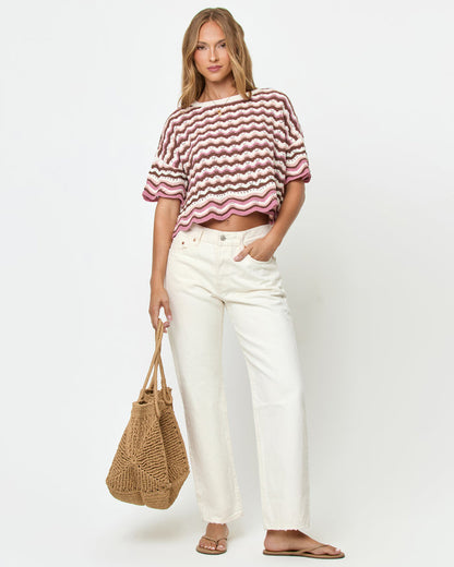 Front view on model of the LSPACE Sunchaser Top in Neapolitan, a short-sleeve crochet top in a brown, pink, and white wave pattern with scalloped hem, styled with white wide-leg jeans and a straw tote bag.