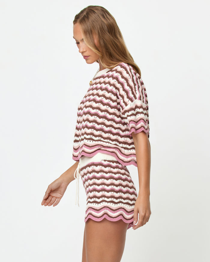 Side view on model of the LSPACE Sunchaser Top in Neapolitan, a short-sleeve crochet top in a brown, pink, and white wave pattern with scalloped hem, styled as a set with the matching Sunchaser Short.