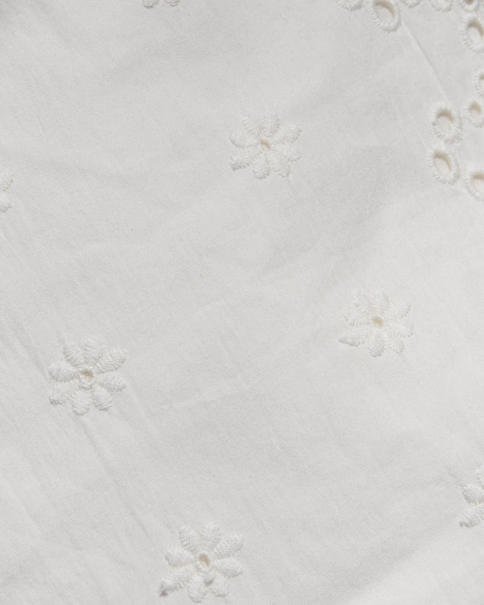 Close-up of a white fabric with delicate floral eyelet embroidery and small cutout details.