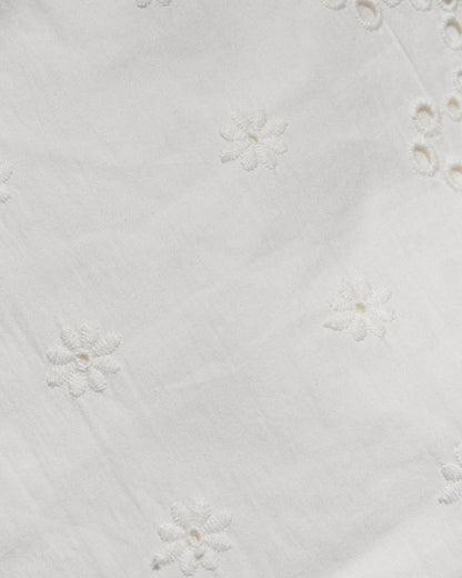 Close-up of a white fabric with delicate floral eyelet embroidery and small cutout details.