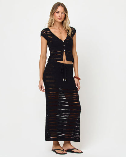 Side view of model wearing the LSPACE Tula Top in black, a semi-sheer crochet cropped top with cap sleeves with the mathcing Skirt.