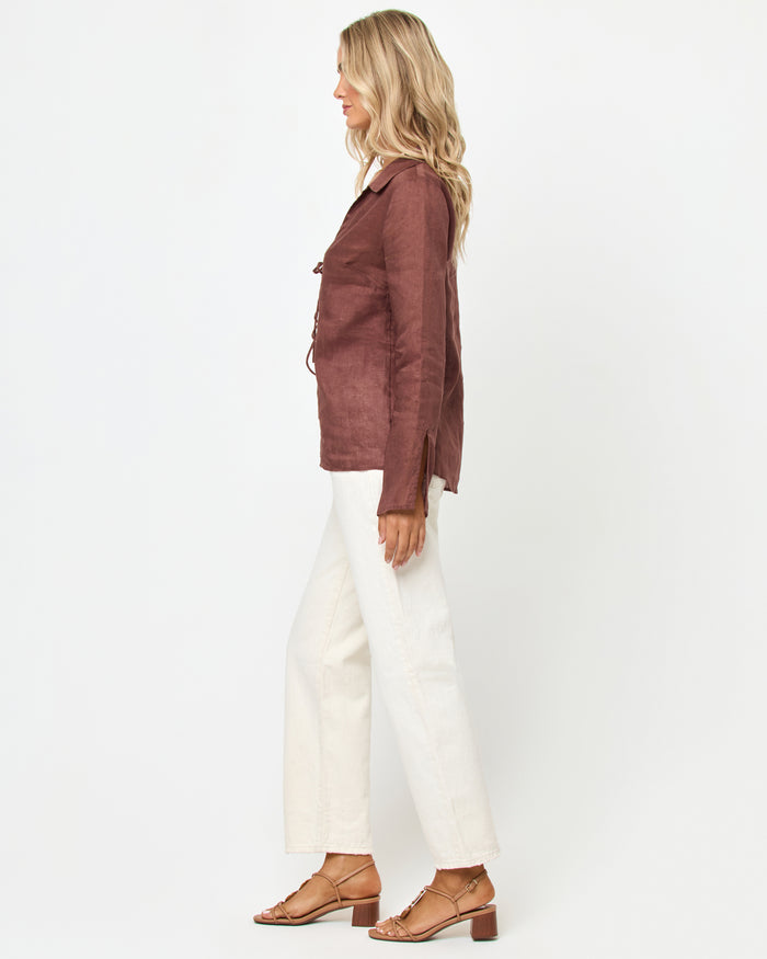 Side view of a model wearing the LSPACE Venice Shirt in cafe, showing the linen construction, tie front closures, and side slits, styled with white wide-leg pants.
