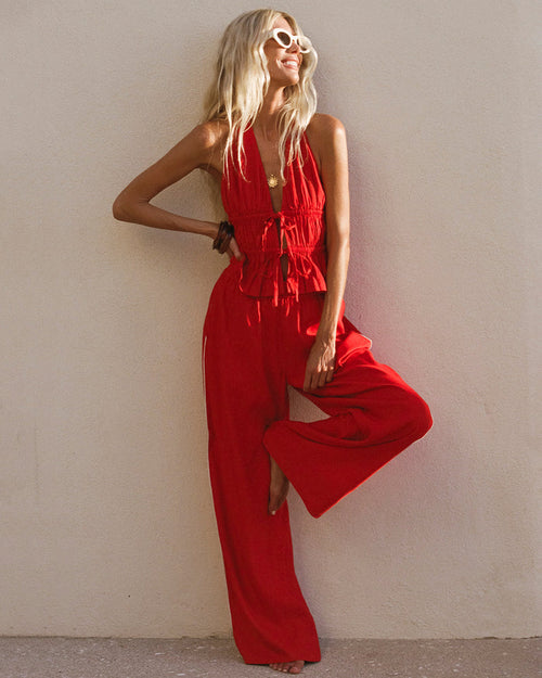 Front view of a model wearing the LSPACE x The Salty Blonde Sur Pant in flame-cream, wide-leg flowy pants in flame red with a cream side-seam stripe, styled with a matching red halter top in an outdoor setting.