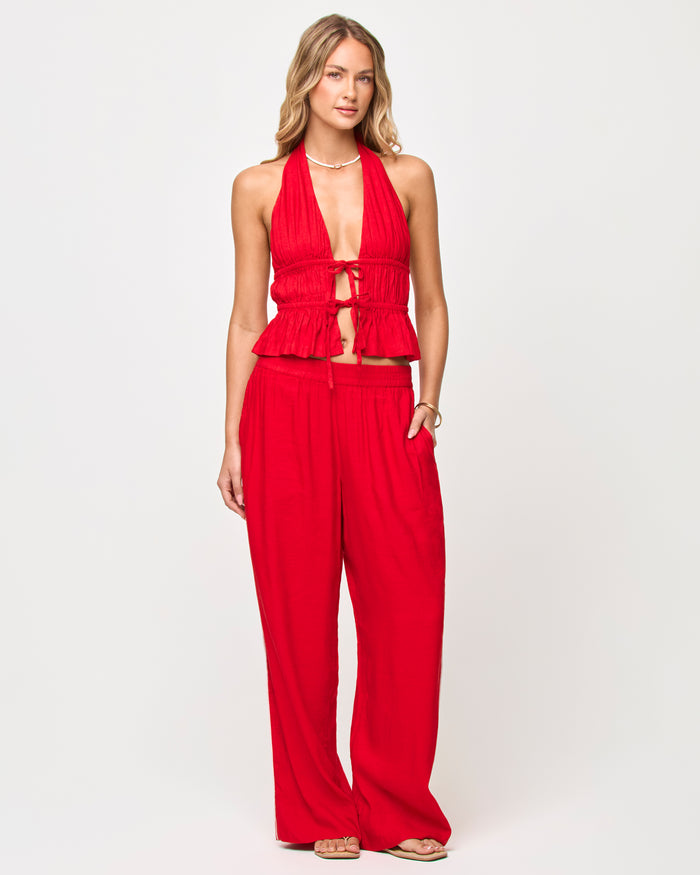 Front view of a model wearing the LSPACE x The Salty Blonde Sur Pant in flame-cream, wide-leg high-waist pants in flame red with an elasticized waistband, styled with a matching red halter top.