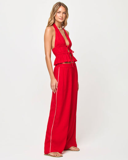 Side view of a model wearing the LSPACE x The Salty Blonde Sur Pant in flame-cream, showing the wide-leg silhouette and cream side-seam stripe detail on the flame red fabric, styled with a matching halter top.